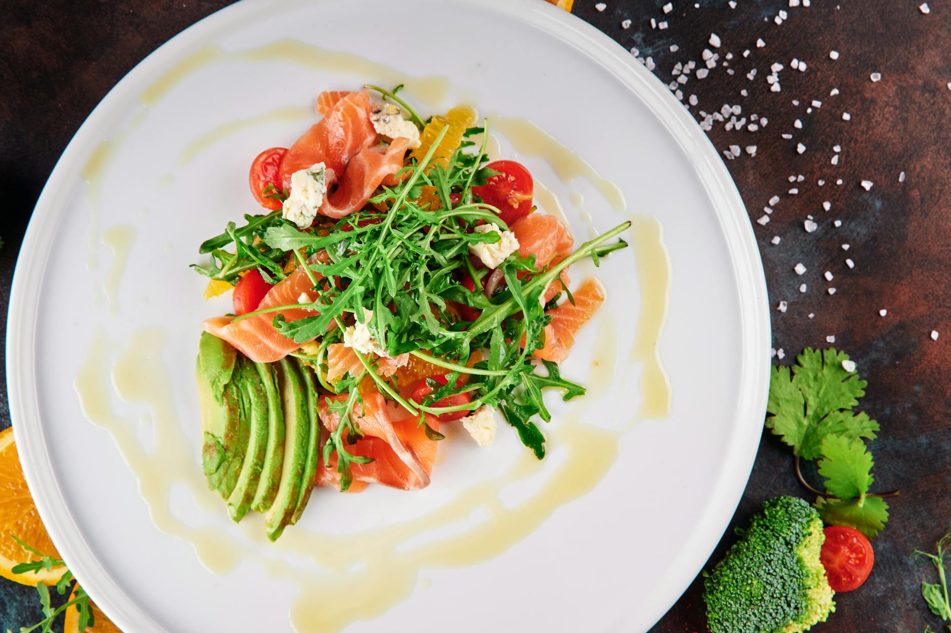 A top-view shot of a vibrant salmon and avocado salad with arugula, cherry tomatoes, and feta cheese.