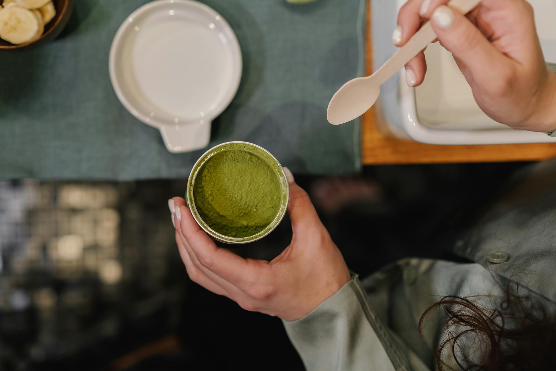 A person holding a container of matcha powder with a spoon, ready for use.