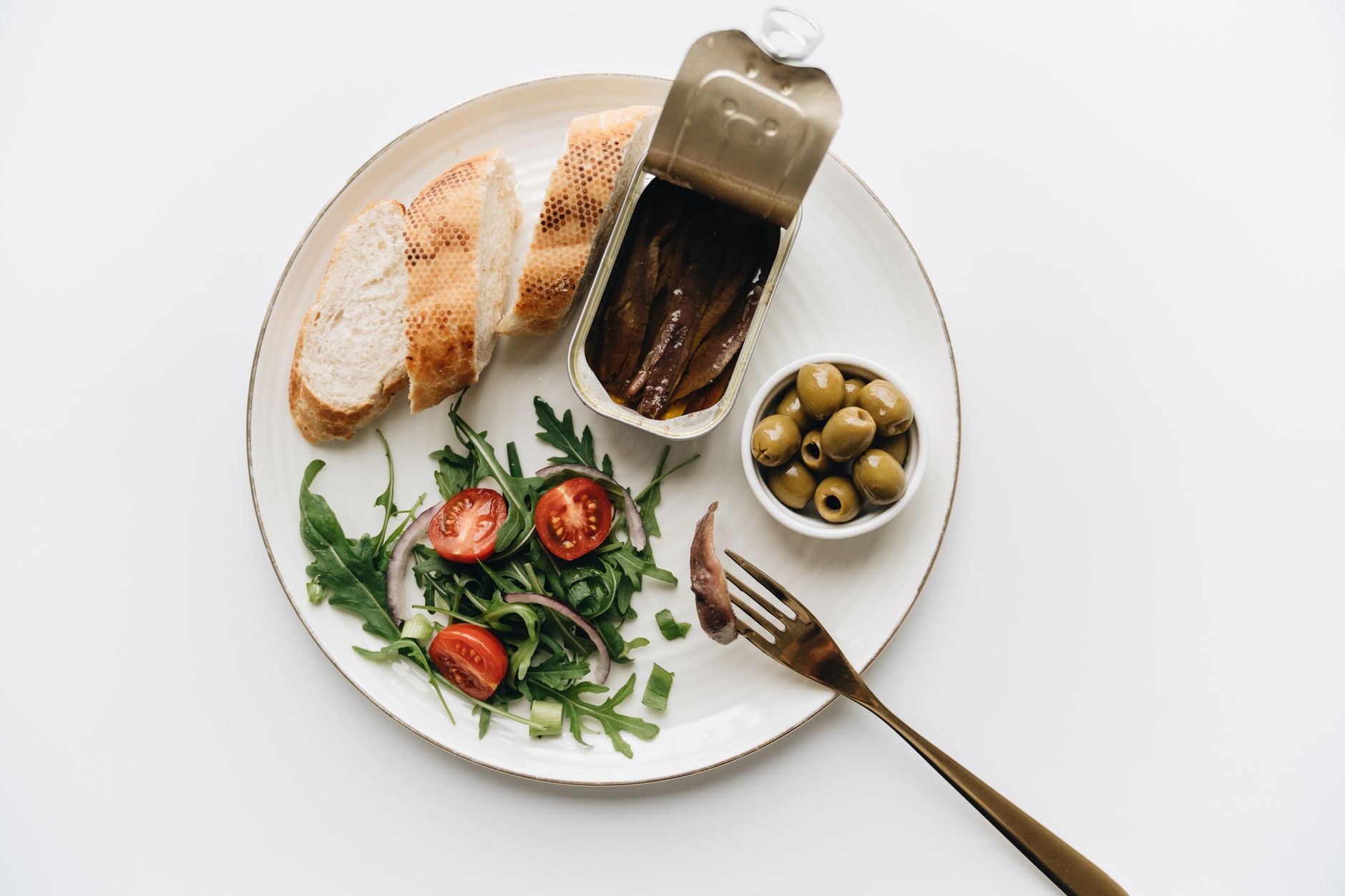 A gourmet Mediterranean dish featuring anchovies, olives, bread, and fresh salad on a plate.