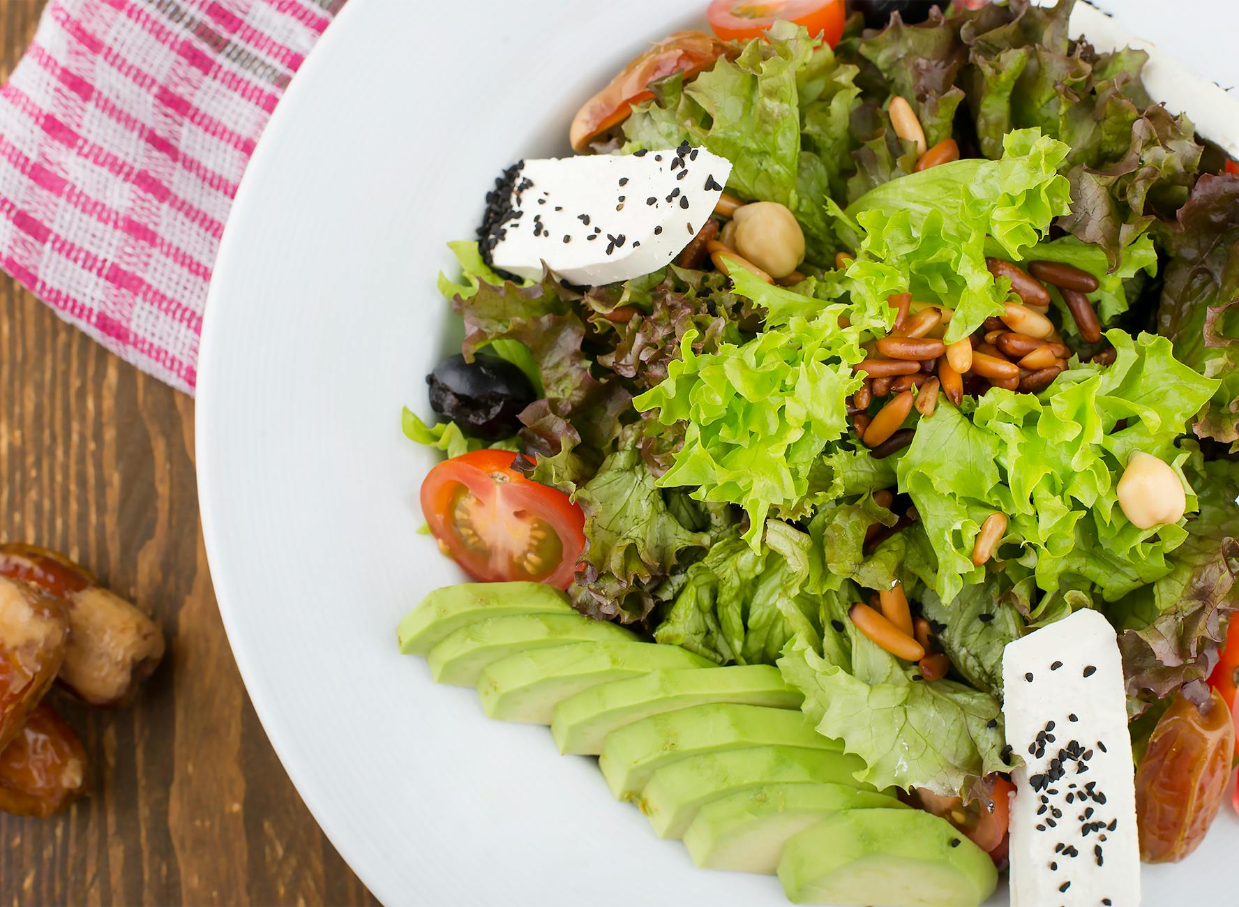 A vibrant salad featuring fresh lettuce, avocado slices, cherry tomatoes, pine nuts, and cheese, perfect for a healthy meal.