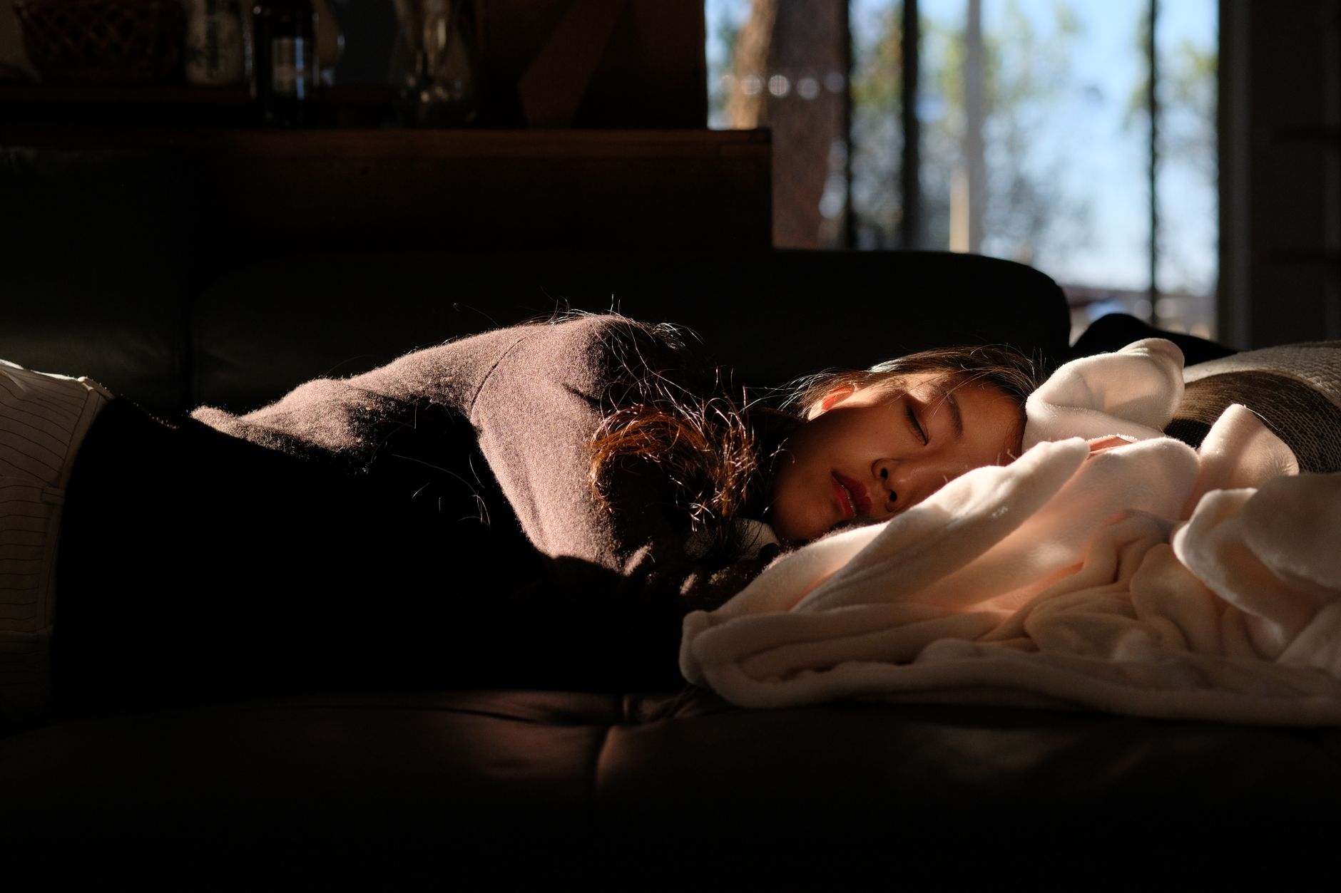 A woman peacefully sleeping on a couch under warm sunlight streaming through the window.