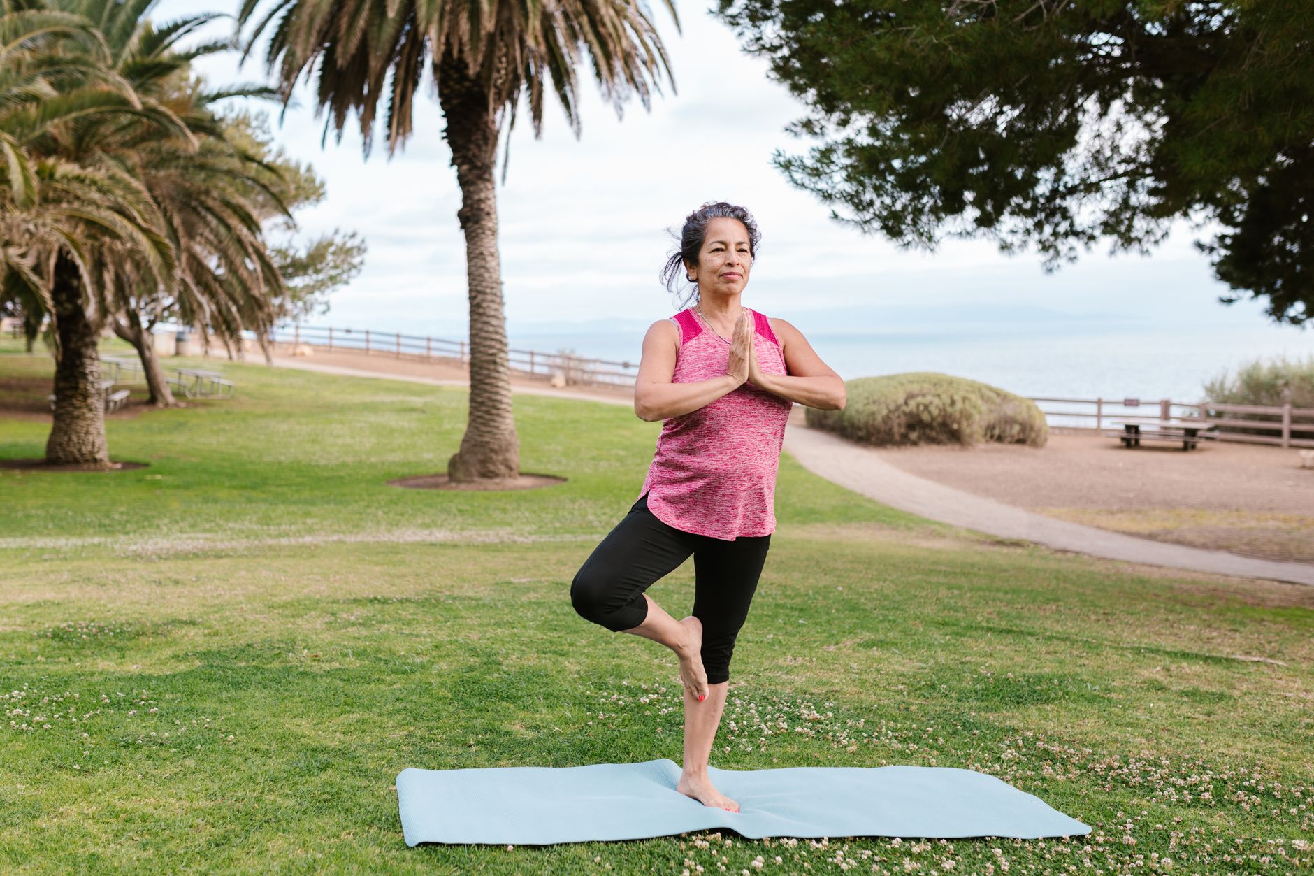 Elderly woman doing yoga on a mat in a park, embracing fitness and tranquility.