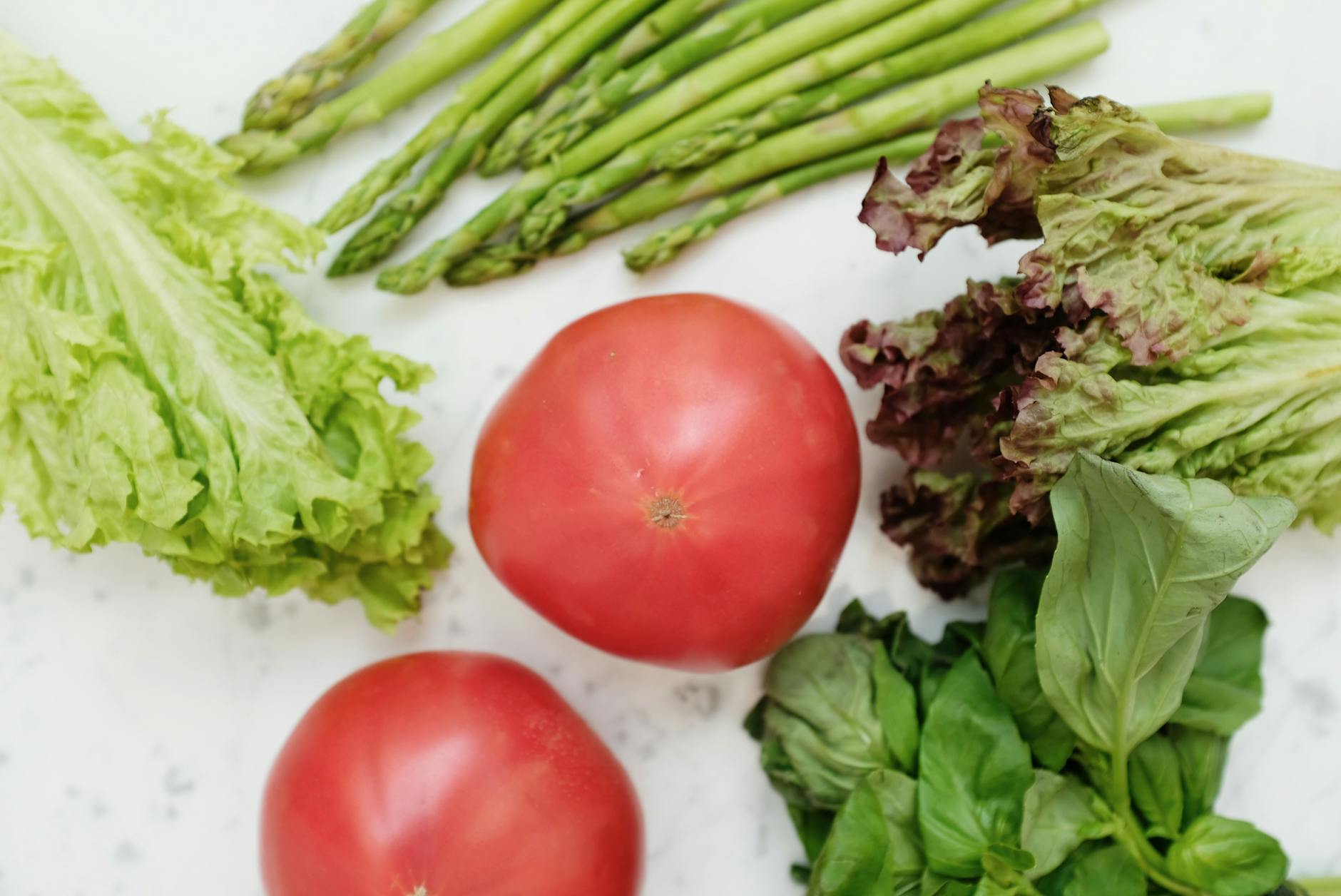 Top view of fresh asparagus, lettuce, basil, and tomatoes, highlighting healthy and nutritious ingredients.