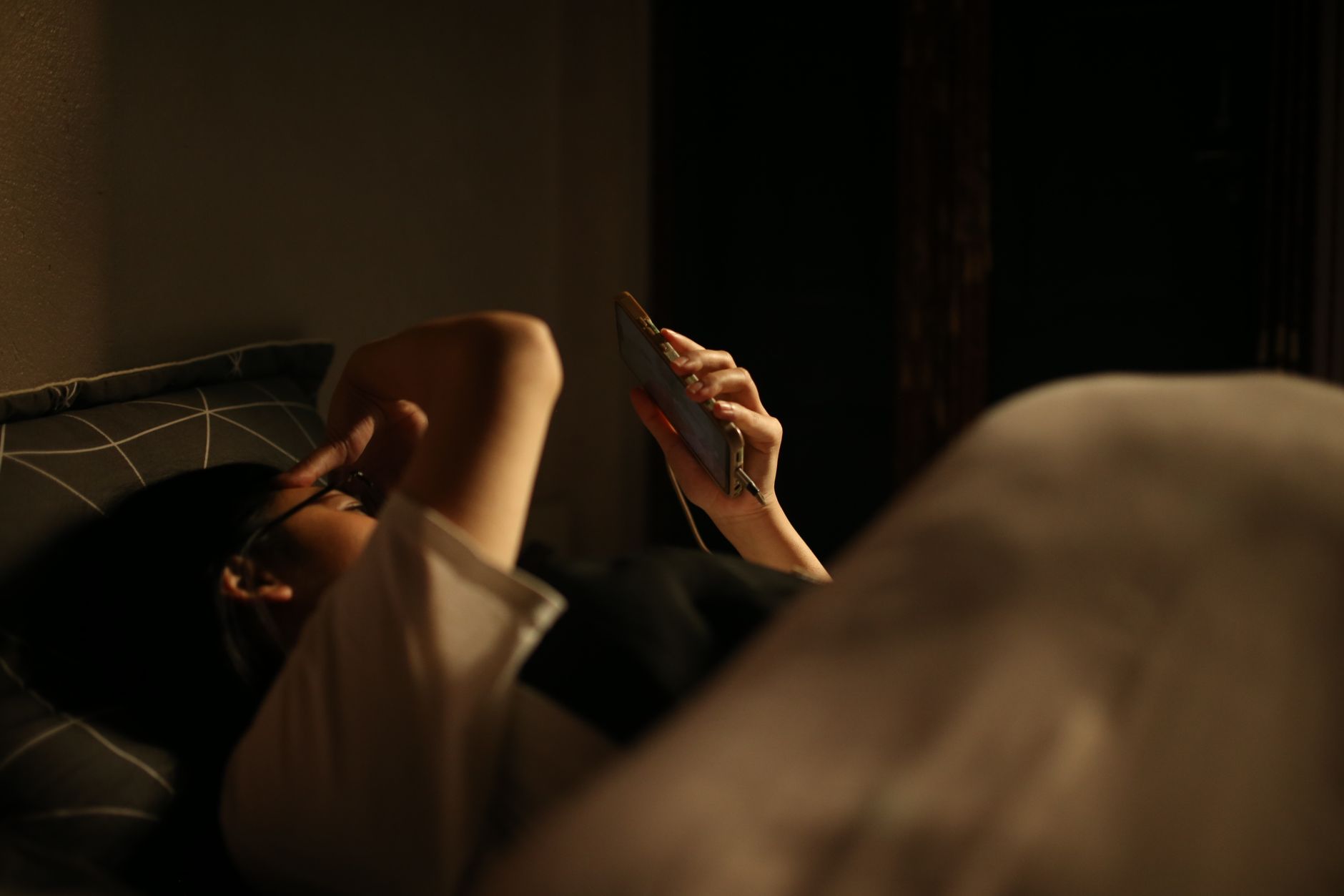 A woman lying on a bed, browsing her phone in a dimly lit room, capturing a moment of relaxation.