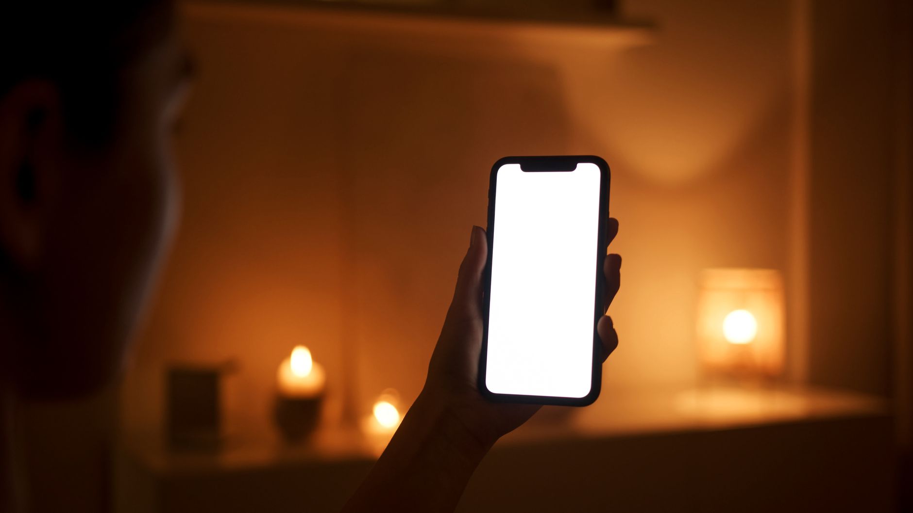 A person holding a smartphone in a cozy, candlelit room, emphasizing modern technology use in warm settings.