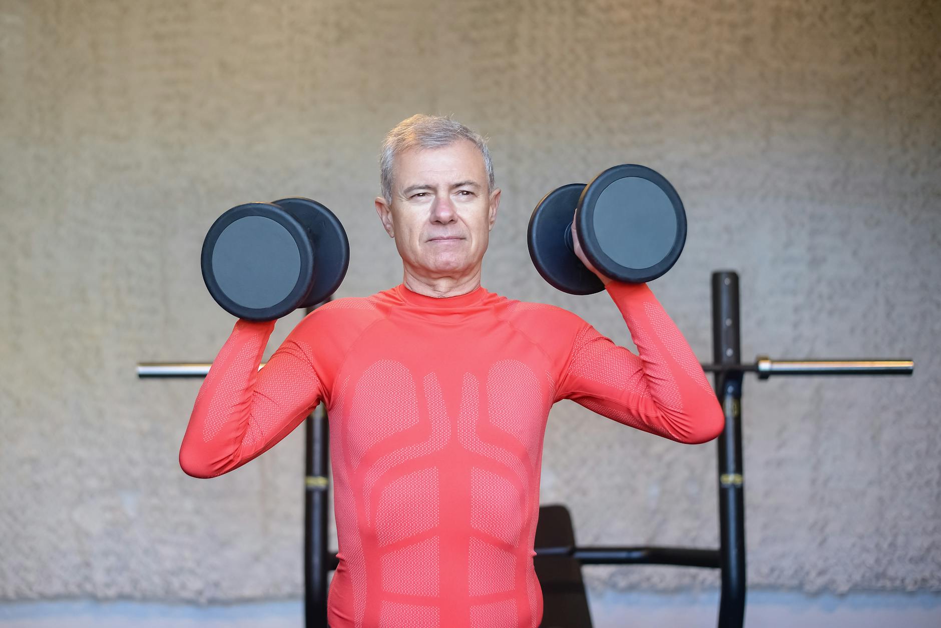 Senior man in vibrant red outfit weightlifting indoors, promoting fitness and healthy lifestyle.