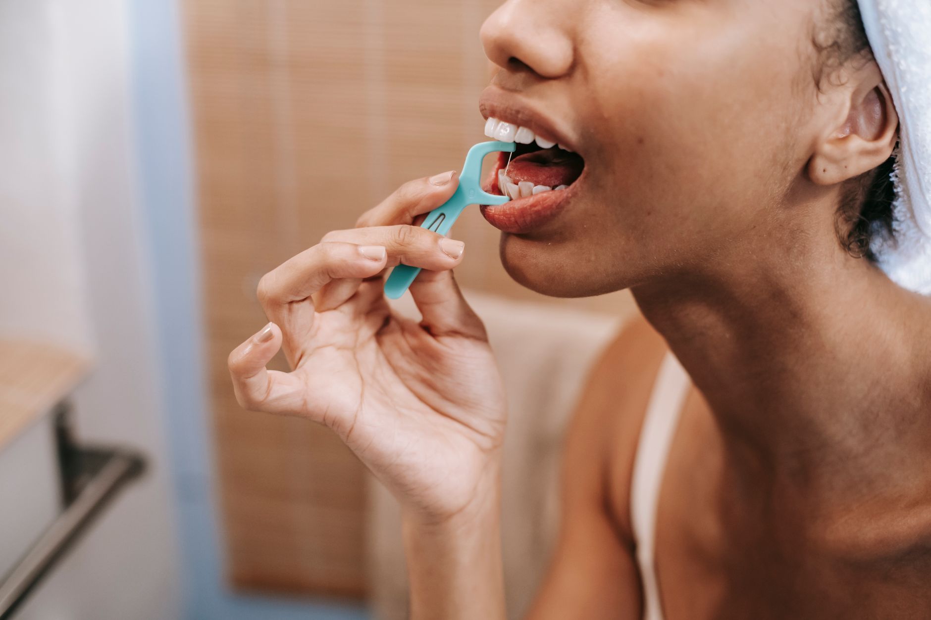 Crop ethnic female doing oral procedure with dental flosser in morning at home